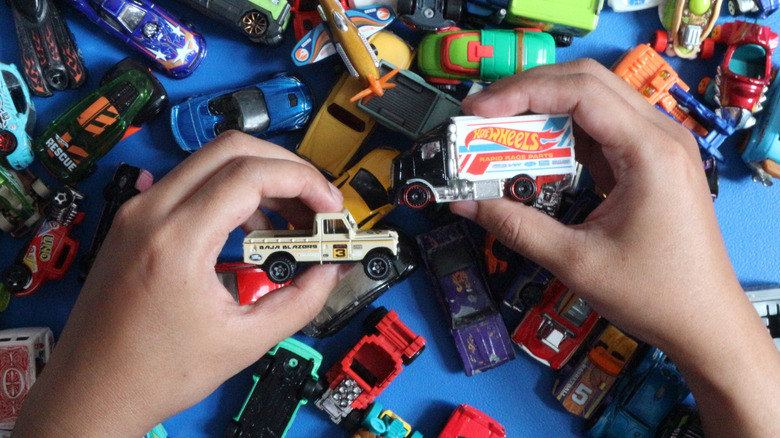 A collection of Hot Wheels cars of different styles ad colors with a pair of hands holding two of the cars.