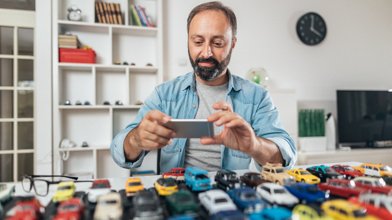 A man using a cell phone to take a picture of a collection of toy cars.