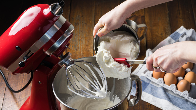 Person pouring mixture into a KitchenAid stand mixer.