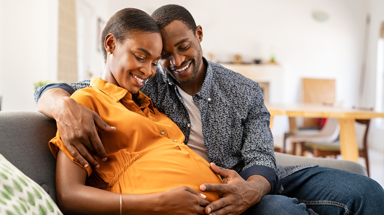 Husband and pregnant woman hugging belly at home