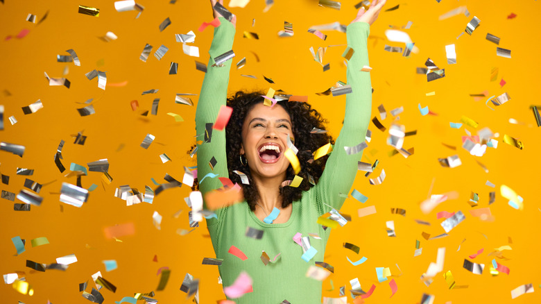 Woman Celebrating Big Win Showered In Tinsel Confetti On Yellow Background