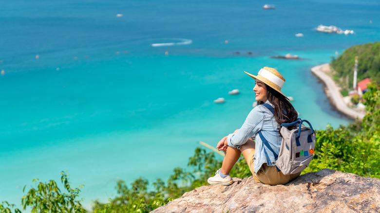 Woman sitting on top of rock, gazing at ocean