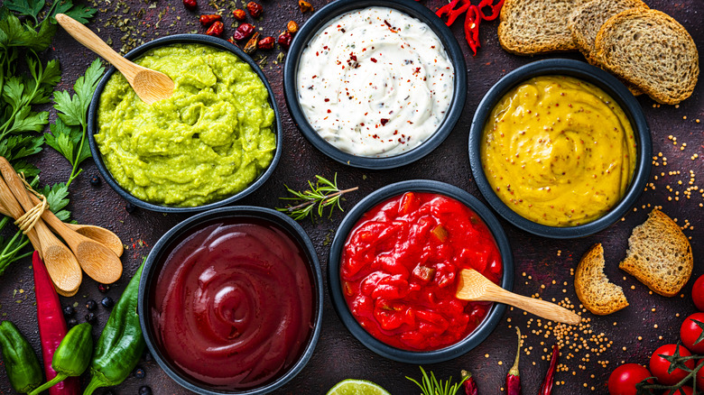 Set of five dip sauces shot from above on dark table