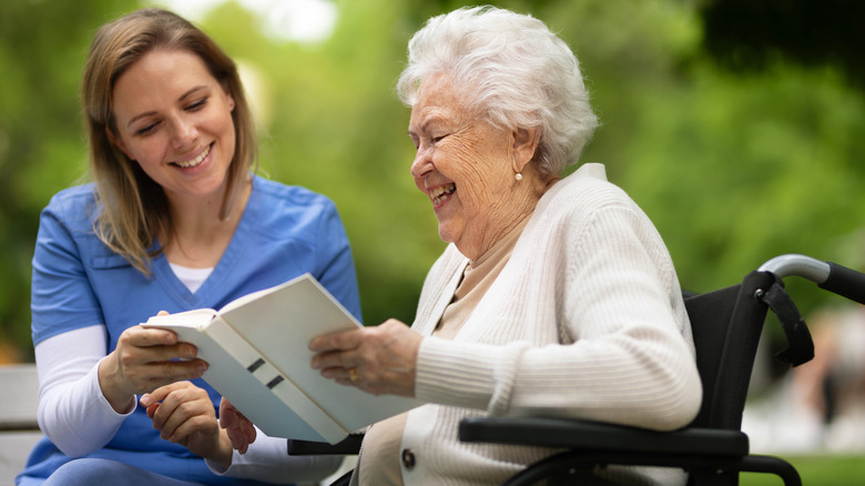 A smiling elderly woman reading a book in a wheelchair