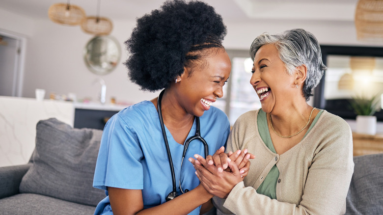 A nurse and elderly woman holding hands and laughing