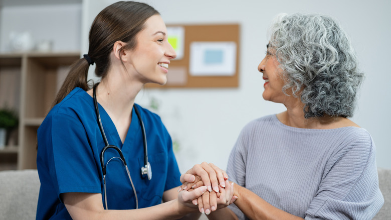 A nurse and an elderly woman holding hands and smiling