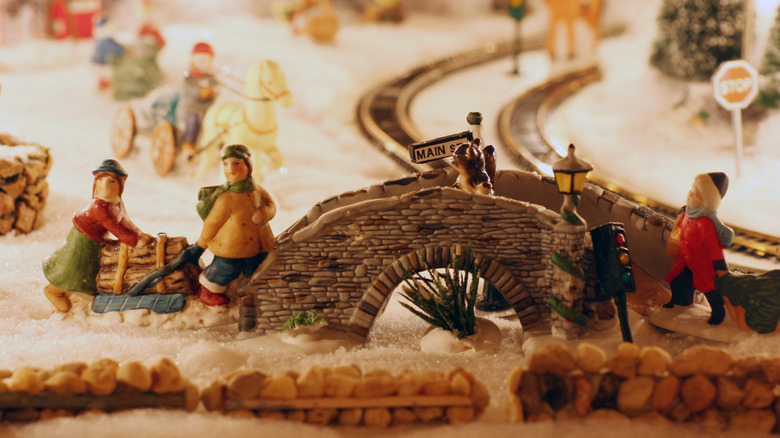 A Department 56 Christmas village scene featuring a charming bridge and ceramic villagers lugging firewood.