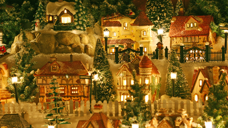 A charming, glowing display of Department 56 Christmas village buildings, interspersed with pine dollhouse trees, on a blanket of batting-made snow.