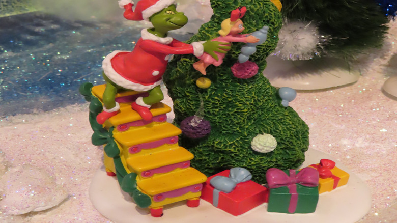 Close-up of a Grinch Village figurine from Department 56, featuring the Grinch helping Cindy hang an ornament on the tree.