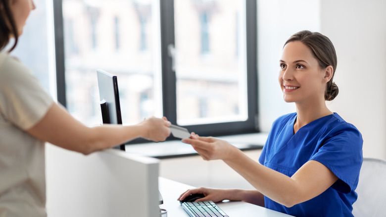 A smiling nurse taking a medicare card from a patient