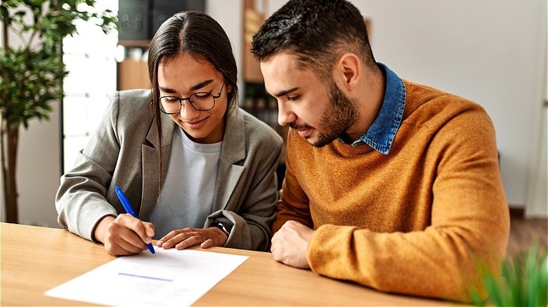 Smiling couple reviewing, signing document