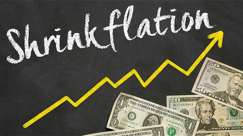 The word 'shrinkflation' written on board with an arrow and U.S. banknotes beneath it