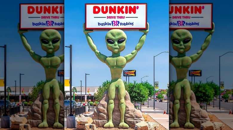 New Mexico alien holds up a Dunkin' Donuts and Baskin Robbins Drive Thru sign.