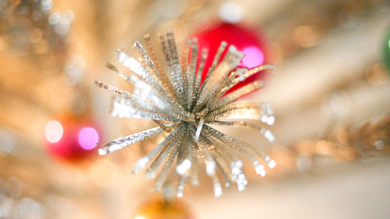 A sparkling silver pom pom on the edge of a vintage aluminum Christmas tree.