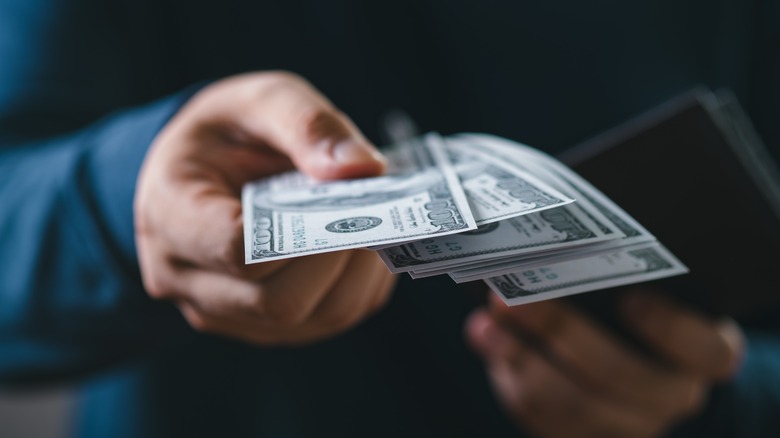 Close-up of a person handing over US dollar bills.