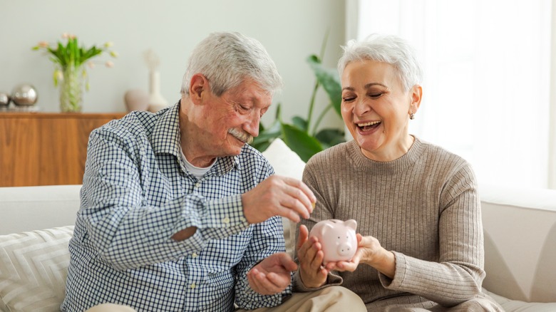 Adult mature couple holding piggy bank putting money coin