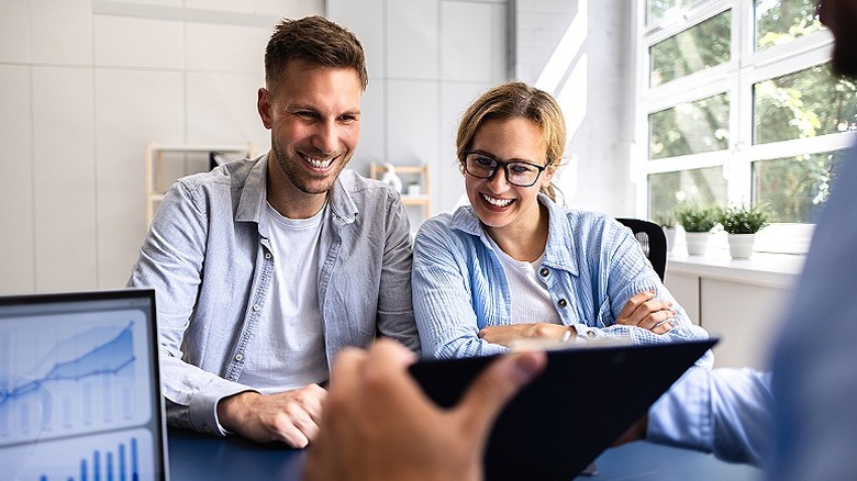 Couple smiles while looking at data analysis presented to them on a tablet