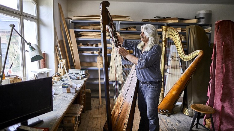 A man repairing a harp in a room with other harps