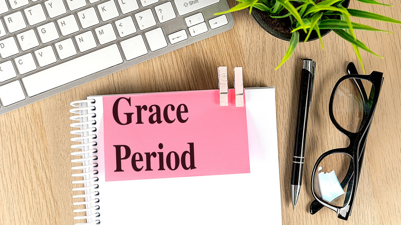 A pink sticky note reading "Grace Period" attached to a notebook with a keyboard, pen, and glasses in the background.