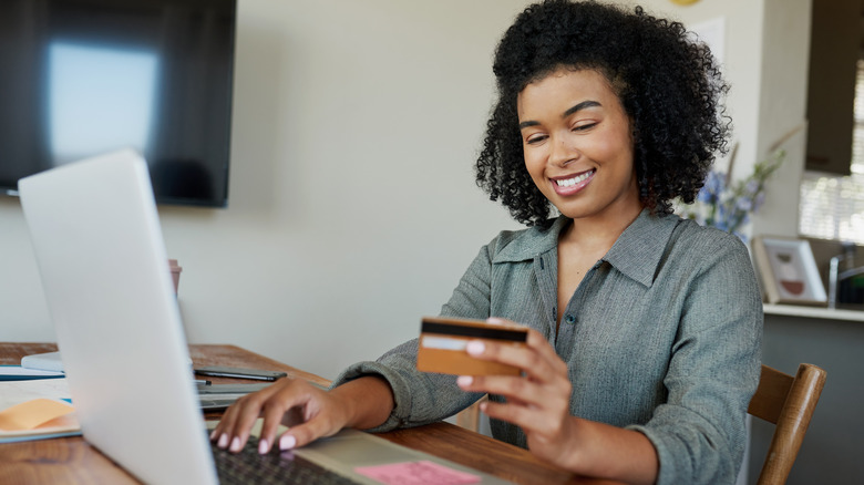 A woman holding a credit card in one hand and typing on a laptop with the other.