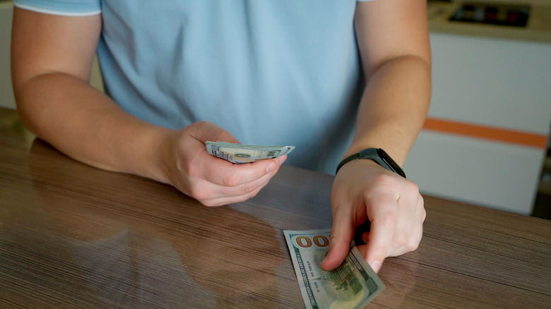 A young man in a blue polo shirt is counting wages