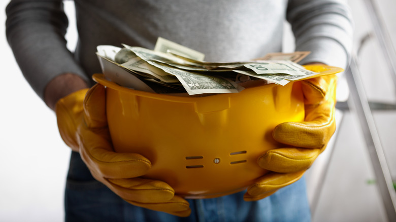 A person holding a yellow hardhat full of dollar bills