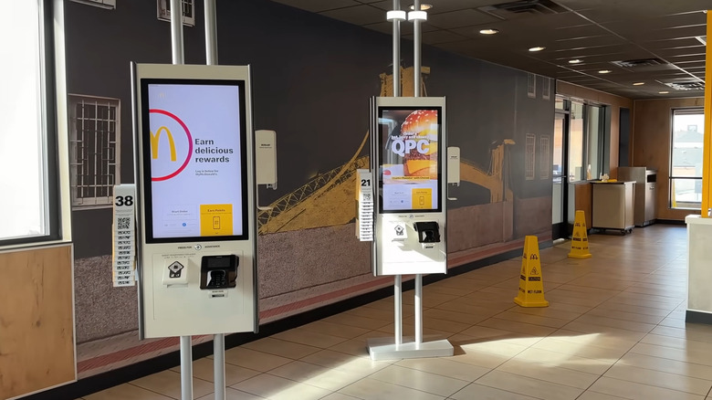 A pair of McDonald's order touchscreen kiosks in a sunny store.