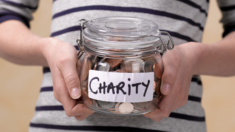 A person holding a jar of coins labeled 'Charity.'