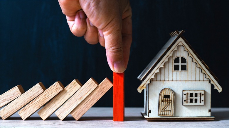 Hand holding a red block to stop falling blocks from hitting house figure