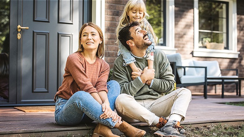 Family of three smiles as they sit on their front porch