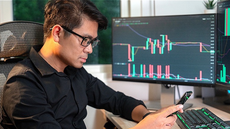 Person in front of computer monitors at home looking at phone