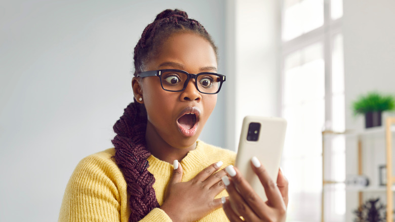 Woman looks at mobile phone with surprised open mouthed expression