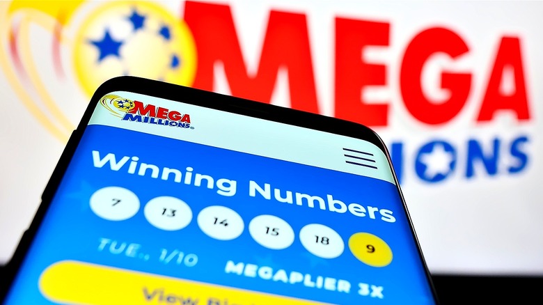 Phone showing winning Mega Millions numbers in front of white Mega Millions sign