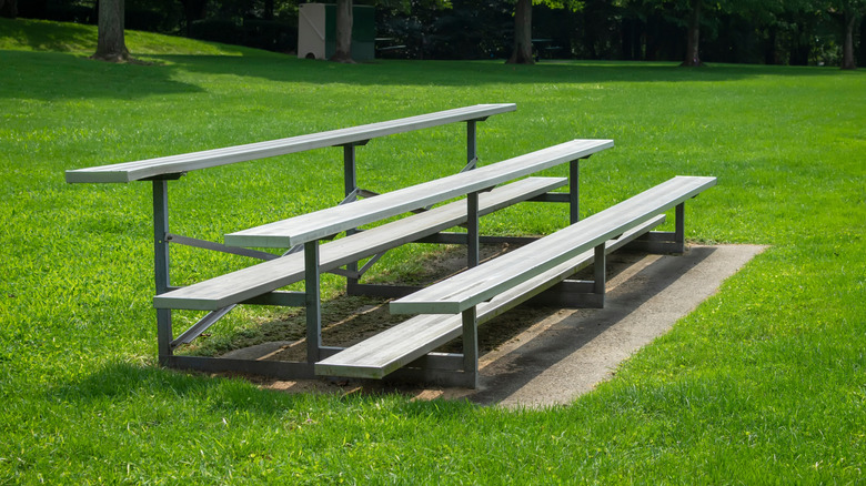 A small set of aluminum bleachers on a sunny day, against a bright park green.