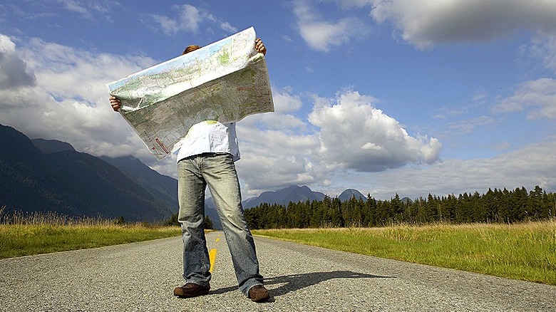 Person looking at map in the middle of an empty road with a cloud-filled sky