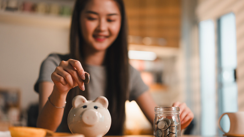 a young woman putting coins into a piggy bank