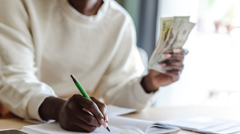 man holding dollar bills while writing in a book