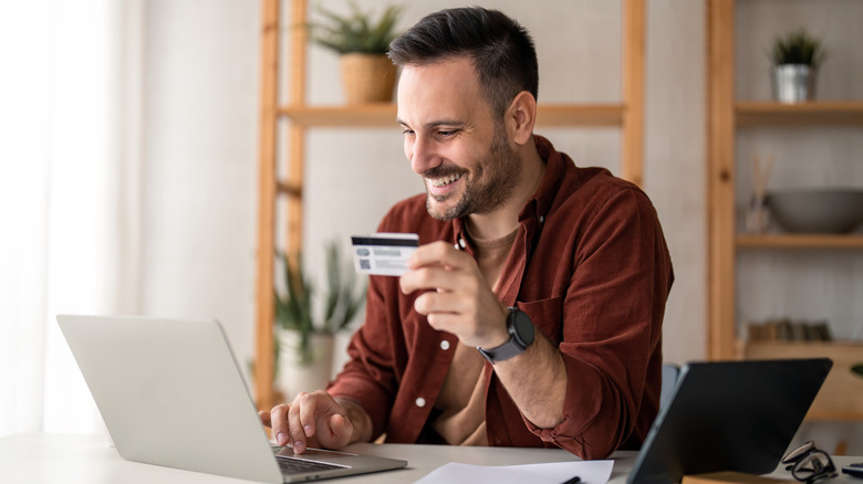 man holding a credit card while smiling at a laptop