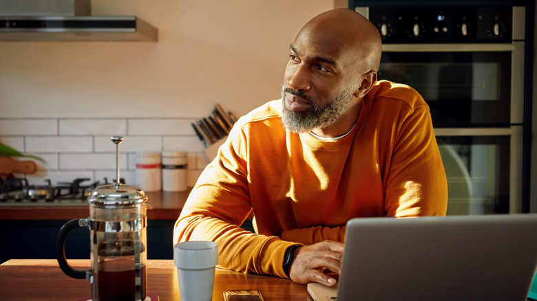 man stares offscreen with a laptop on the table