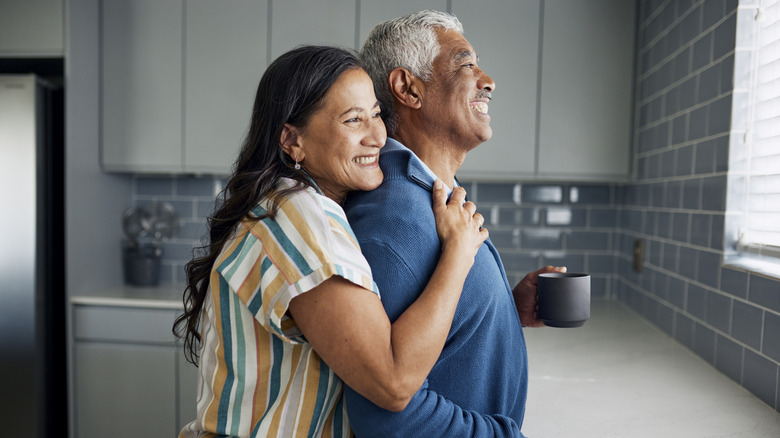 An elderly couple is drinking coffee and gazing out the kitchen window.