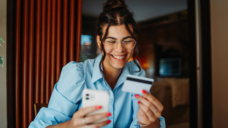 A smiling woman holding a credit card and smart phone