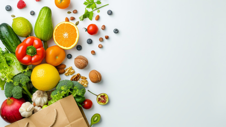 A paper bag full of fruits, vegetables and nuts on a white background