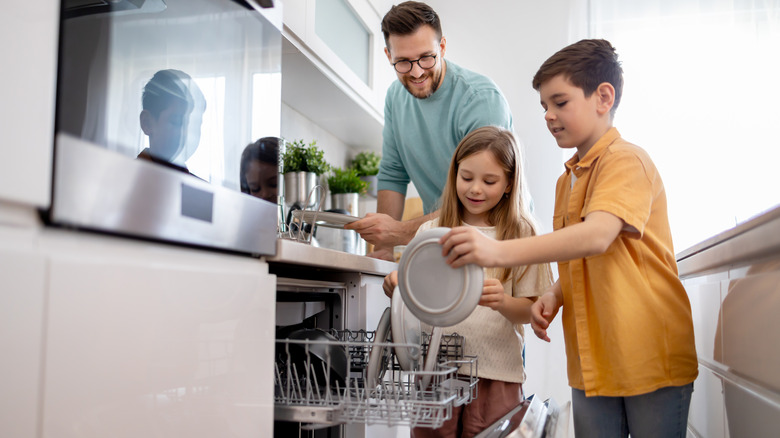 A smiling man with a young girl and boy loading a dishwasher