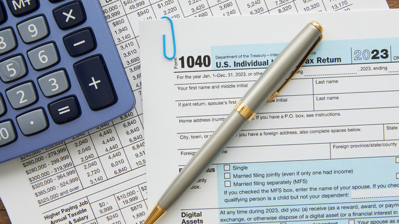 A U.S. tax form 1040 with a pen sitting atop it and a calculator in the background.