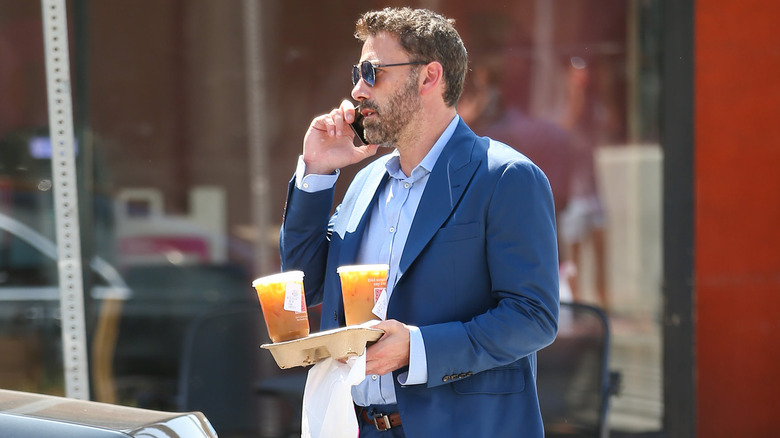 Ben Affleck chats on cell phone while holding a Dunkin' Donuts drink tray and bag.