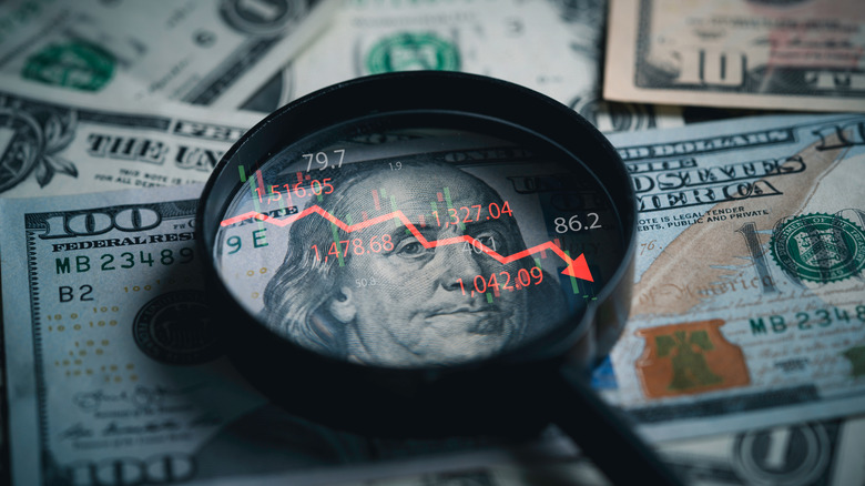 magnifying glass showing downward trend line on $100 bill