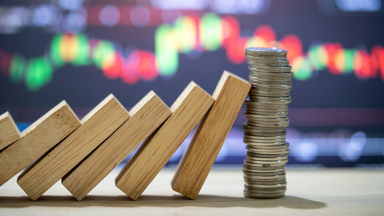 dominoes falling into stack of coins in front of stock chart