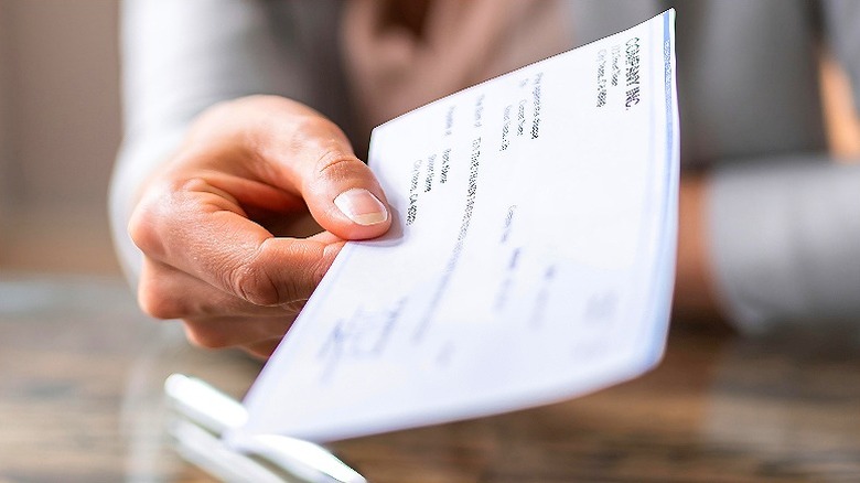 Hand extended forward toward screen, holding a paycheck