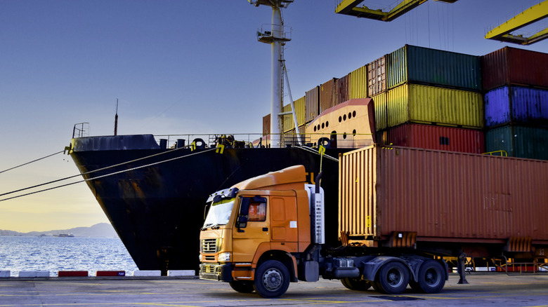 Commercial truck hauling shipping container away from ship in port