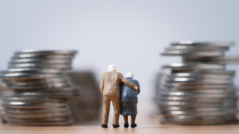 Miniature elderly couple standing by stacks of coins